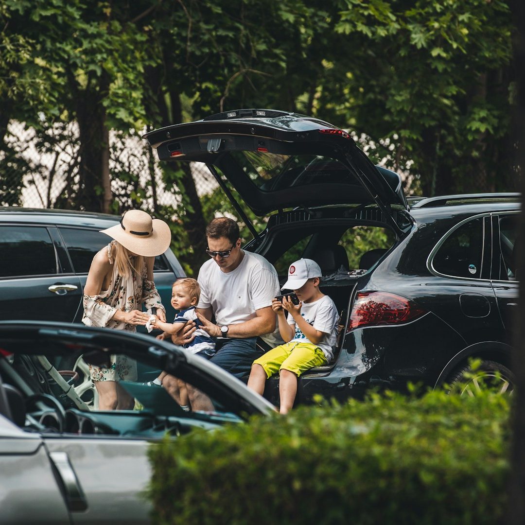 Crystal Cars Airport Transfer Passengers Enjoying A family sitting by a car with children, enjoying a relaxed outdoor moment.