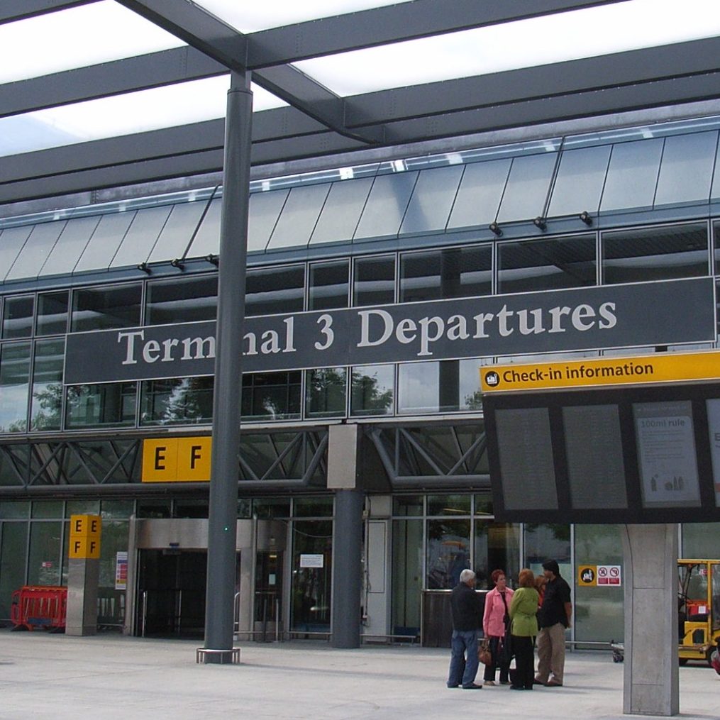 Heathrow Airport On Time Taxi Cab Service A person wearing a mask walks through Heathrow Airport, pulling a suitcase.