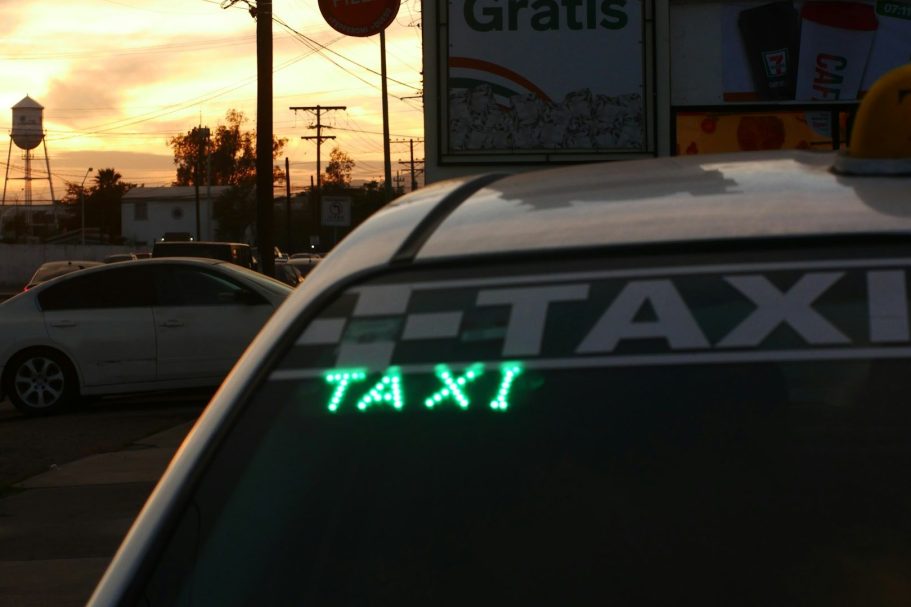 Fixed Fair Airport Transfers Taxi sign illuminated on top of a vehicle, with a sunset in the background.