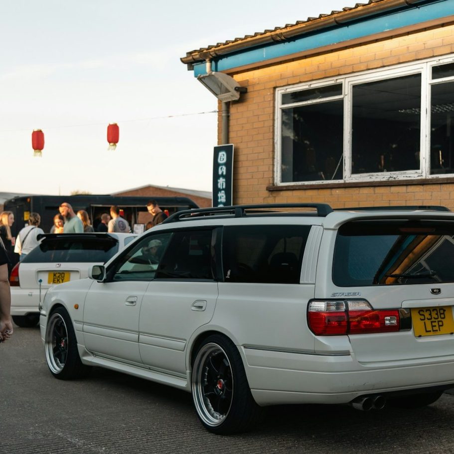Estate Cars for Airport Transfer Two white cars were parked outside a building with a gathering of people nearby.