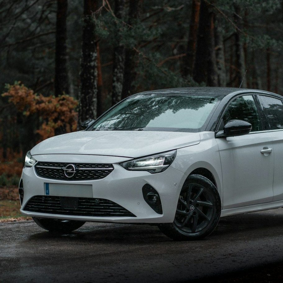 Saloon Car for Airport Transfer White compact car parked on a forest road surrounded by trees.