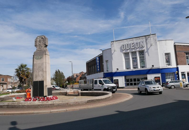 Taxi Service in Beckenham, BR3 A war memorial surrounded by flowers, with a building and vehicles nearby.